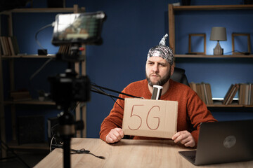 Strange man in a protective foil cap holding banner with 5g message. filming commercial video vlog,...