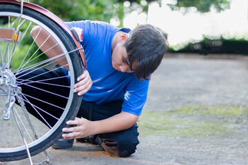 Asian child in blue t-shirt holding front wheel and checking it before riding in front of his...