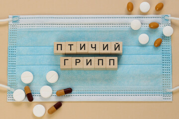 Птичий грипп - avian influenza in Russian, spelled with wooden cubes on a surgical mask with scattered pills around.