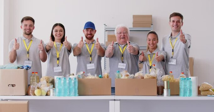 A group of happy volunteers standing in a row showing a thumbs up. People of all ages participate in charitable giving. Concept volunteer opportunities, pack food in volunteering center