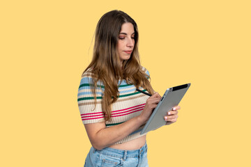Young woman drawing on tablet with stylus on yellow background