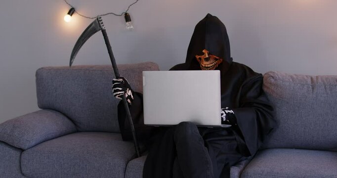 Grim reaper, holding a scythe and wearing a devilish mask, uses a laptop while sitting on a sofa. This nightmare blends horror with the everyday use of the internet and online technologies.