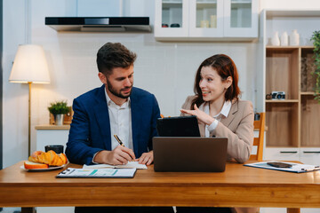 Business documents at kitchen modern office table with tablet and laptop computer and chart and two colleagues working a project or reviewing and discussing a business project.