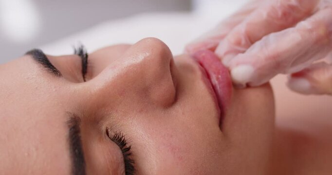 Close up of cosmetologist doctor examining young woman lips condition before injections with syringe for augmentation, anti wrinkle or correction procedure in cosmetology beauty salon. 4k video.