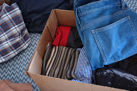 Sorting clothes for donations. Cardboard donation box with things.