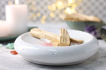 Palo santo sticks, gemstones and burning candle on light grey textured table, closeup