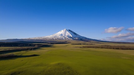 Fototapeta premium Aerial drone view of a snow-capped volcano with green field at summer