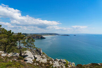 Fototapeta premium Vue panoramique des plages de la baie de Douarnenez depuis les falaises de la presqu'île de Crozon, sous un ciel bleu parsemé de nuages blancs. Un paysage côtier typique de la Bretagne.