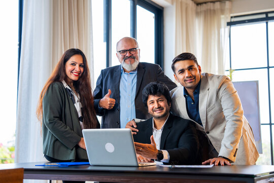 Indian asian Corporate professionals smiling confidently, woman on laptop, others showing thumbs up