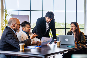 Group of Indian professionals in formal attire working with documents and laptop, discussing ideas