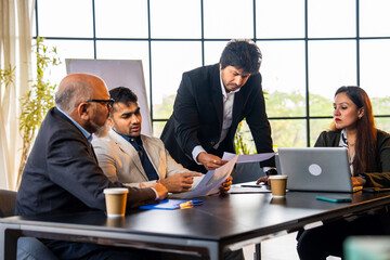 Group of Indian professionals in formal attire working with documents and laptop, discussing ideas
