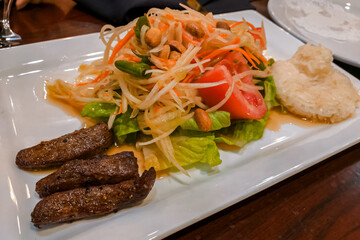 Thai green papaya salad (Som Tum) with grilled pork and sticky rice. Spicy, sweet, and savory Thai dish. Ideal for Thai food blogs, restaurant menus, and culinary publications.
