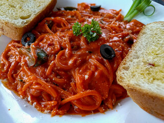 Spaghetti alla puttanesca with bread. Tomato-based sauce with olives, capers, and anchovies. Flavorful Italian pasta dish. Ideal for Italian food blogs, restaurant menus, and culinary publications.