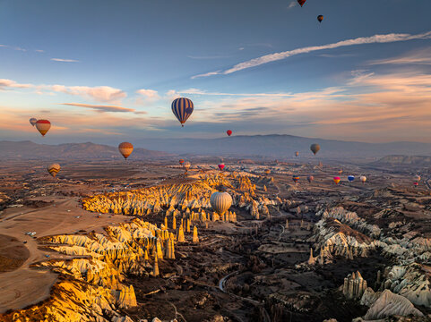 Aerial drone view of the classic scene: hot air balloons floating above Love Valley with towering rock formations resembling chimneys or phalluses at sunrise in Cappadocia