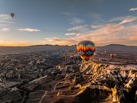 Aerial drone view of a colorful hot air balloon floating above Love Valley with towering rock formations resembling chimneys or phalluses at sunrise in Cappadocia