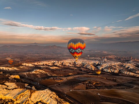 Aerial drone view of a colorful hot air balloon floating above Love Valley with towering rock formations resembling chimneys or phalluses at sunrise in Cappadocia