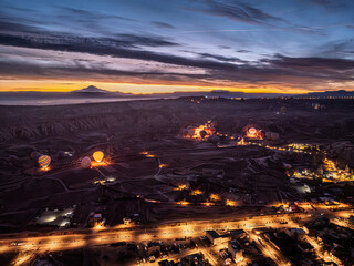 Aerial drone view of Göreme with lights on at dusk during sunrise, with hot air balloons preparing...