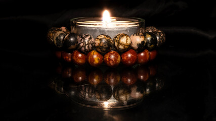 Candlelight with decorative beaded bracelet on reflective surface