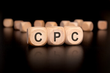 wooden cubes with black letters forming the acronym -CPC on a dark reflective surface