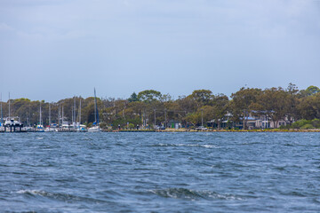 A scenic waterfront view of Raymond Island in Victoria. Moored boats dot the lake waters of the inlet, a small regional coastal town at Paynesville, Australia.