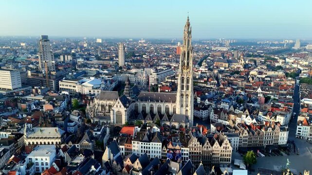 cityscape of Antwerp unfolds, dominated by the iconic spire of the Cathedral of Our Lady, rising majestically above a mix of historic and modern architecture under a clear, early morning sky