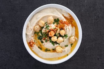 Chickpea hummus with olive oil, parsley and paprika in bowl on black background