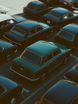 Fototapeta Sea of Cars: A captivating aerial view showcases a dense parking lot filled with a multitude of vintage and classic cars, their dark, glossy surfaces reflecting the ambient light.
