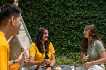 A group of Asian friends enjoying a casual outdoor picnic, holding drinks and engaged in a lively...