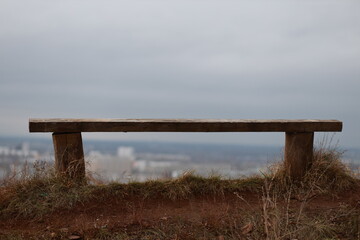 Obraz premium Wooden bench is sitting on a hillside with a view of the city below