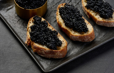 Black caviar on pieces of bread on black table, top view