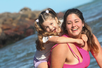 Obraz premium young cheerful hispanic mother and her little daughter in the water at the beach on sunny summer day