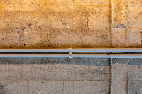 Industrial wall featuring raw concrete with visible textures and imperfections, complemented by two parallel pipes running horizontally across the surface. 