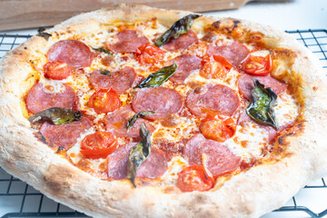 Raw pepperoni pizza is ready to cook. Pizza with sausage, tomatoes, cheese and basil on a baking rack.
