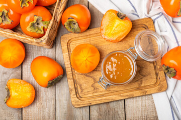 Persimmon jam with slices of ripe persimmon on wooden textured table. Delicious persimmon jam. Marmalade. Healthy sweets. Vegan. Close-up. Space for text. Copy space.