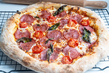 Raw pepperoni pizza is ready to cook. Pizza with sausage, tomatoes, cheese and basil on a baking rack.