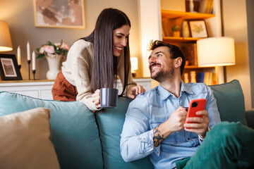 Couple reading online news using smart phone and drinking morning coffee at home