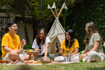 A diverse group of Asian friends enjoying a cheerful outdoor picnic with drinks and snacks. They...