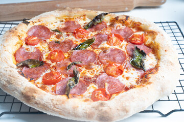 Pepperoni pizza with sausage, tomatoes, basil and cheese, with a large toasted rim on a baking dish.