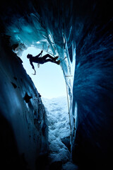 Fototapeta premium Man climbing frozen ice cave in winter mountains