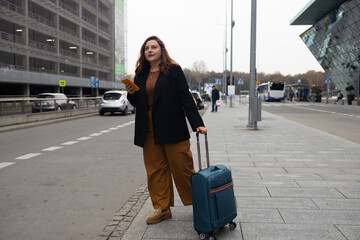 Business smiling 30s lady tourist woman with smart phone in casual clothing taking taxi from an airport. Luggage on the city street. Travel concept.