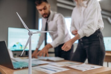 Fototapeta premium Blurred, focused on wind turbine model. Two employees are working in company