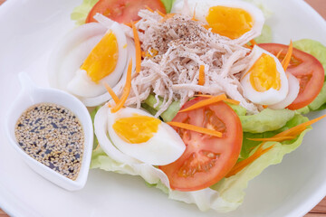 Chicken breast salad, boiled eggs and Japanese sesame dressing in a white ceramic plate. On a pine wood table. Healthy food concepts.