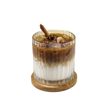 Iced coffee with milk and a cinnamon stick garnish in a textured glass. Layered cold brew latte on a wooden coaster, white background.