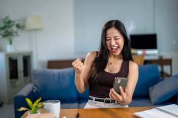 A woman is sitting at a table with a cell phone in her hand, smiling