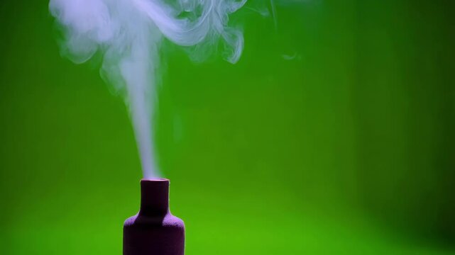 White smoke is billowing and swirling from a small, dark bottle against a vibrant green screen background, creating a dynamic visual effect