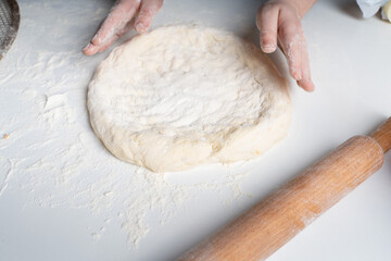 Children's hands show a heart above a circle of dough on a white table. The concept of love for cooking and hobbies.