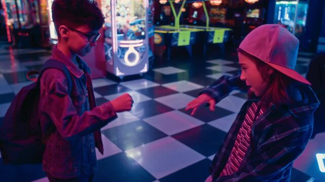 Medium slowmo shot of two young 12-year-old multiethnic boys in casual outfits meeting together at recreation center or gaming arcade, greeting each other, bumping fists