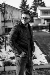 Man in winter gear outdoors. A man wearing sunglasses and a puffer jacket stands confidently in a...