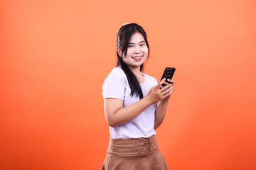 Naklejka premium A smiling person in a white shirt is holding a phone on an orange background