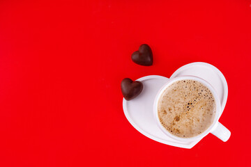 Valentines Day background with cozy sweet romantic atmosphere, candy chocolates, cookie, freshly brewed cup of coffee latte on heart-shaped plate, top view copy space